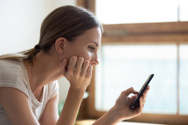 wanita muda duduk di dekat jendela memegang smartphone / iStockphoto